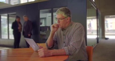 Orta yaşlı bir adam dizüstü bilgisayarın önünde, çenesi çenesinde, ortak çalışma alanında yansıtıcı ifade, iş günü boyunca düşünceli ve analitik bir an düşünüyor.