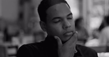 Genç erkek restoran işçisinin siyah ve beyaz yakın plan fotoğrafları. Düşünceli bir ifadeyle çenesini dinlendiriyor. Yumuşak arka plan bulanıklığı, iç gözlem modunda olduğunu gösteriyor.