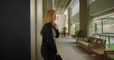 Modern ofis koridorunda duvara yaslanmış koltuklar ve yumuşak bulanık saksılarla yüzünü duygusal bir anda kapatan bir kadın.