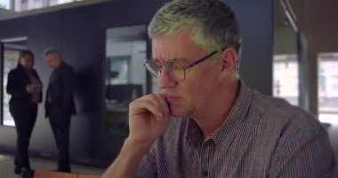 Orta yaşlı, endişeli suratlı, dizüstü bilgisayara bakan, çenesinde dinlenen, ortak ofis alanında oturan gergin ve dalgın görünen bir adama yaklaş.