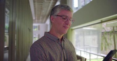 Ofis koridorundaki video görüşmesi sırasında cep telefonu tutan orta yaşlı adama yakın çekim modern çalışma ortamında cep telefonu kullanarak uzaktan iletişim kuruyor.