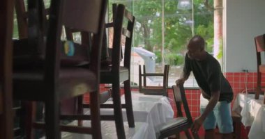 İşçiler, sabah açılış rutini sırasında restoran yemek odasındaki sandalyeleri kaldırıyorlar, sıradan Latin Amerika iç mimarisi.