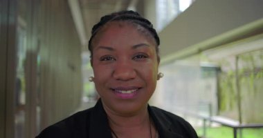 Modern ofis koridorlarında özgüven ve samimiyetle gülümseyen Afro-Amerikan kadınlarının yakın çekimleri profesyonel iş ortamında özgün bir ifade.