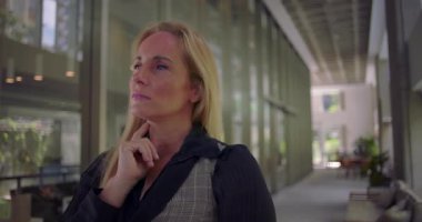 Düşünceli bir şekilde el ele tutuşan bir kadın, fikir ya da kararı düşünürken başını kaldırıp, sessiz bir profesyonel koridorda duruyor.