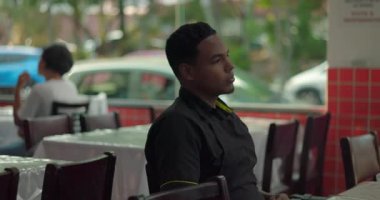 Restoran çalışanı pencere kenarında tek başına oturuyor, vücut dili düşünüyor ve yavaş bir süre boyunca yemek yiyor.