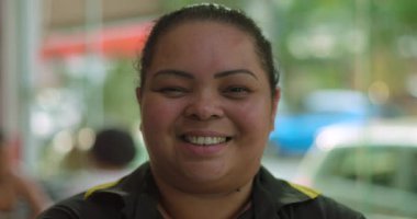 Restoran yemek alanında gülümseyen Latin garsonun yakın çekimi. Kameraya sıcak bir şekilde bakıyor. Arka plan ışığı ve rahat bir atmosfer.