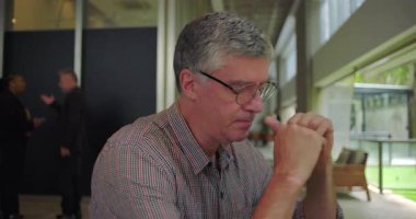 Orta yaşlı bir adam ofis ortamında elleri sımsıkı bağlı, derin düşüncelere dalmış, gelecek ve mesleki belirsizlik kaygılarını dile getiriyor.