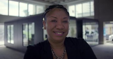 Ofis ortamında gülümseyen Afro-Amerikalı kadın, arkadaş canlısı ifadeyi kapat. Cam pencereler ve iş arka planında kendine güvenen ve sıcak bir varlık.