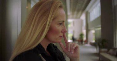 Düşünceli kadın koridorda dinleniyor. Derin düşüncelere dalmış. Modern ofis binasında duvarın önünde duruyor.