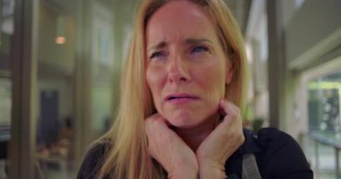 Görünür duygusal sıkıntı içindeki bir kadın, gözleri kapalı ve ağzı titriyor, profesyonel koridorda stres ve kederden derinden etkilenmiş.