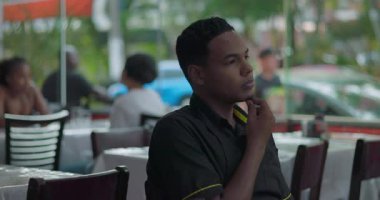 Pencerenin kenarında oturan genç garsonun yan görünüşü derin düşüncelere dalmış, çene üstüne uzanmış, yemek masasındaki sessiz vardiya sırasında dışarıya bakıyor.