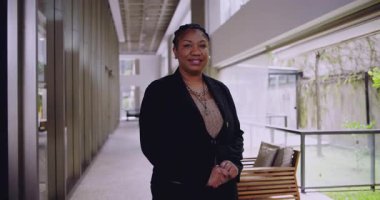 Afro-Amerikalı kadın ofis koridorunda el ele tutuşmuş gülümsüyor nazikçe yaklaşımına sıcak bir şekilde liderlik ediyor ve iş bağlamında güvenini iletiyor.