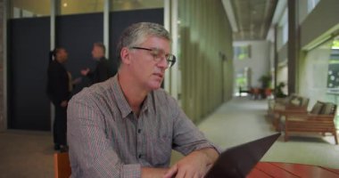 Ofiste yuvarlak masada oturan orta yaşlı bir adam, anlık düşünceli ve endişeli, sonra da gözle görülür endişelerine rağmen laptopta odaklanmış bir kararlılıkla işine devam ediyor.