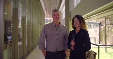 Ofis koridorunda yan yana duran iki profesyonel elinde tablet olan ve gülümseyen bir kadın, gevşek ifadeli bir adam, ikisi de sempatik takım imajı sunuyor.