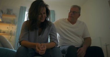 Yatakta oturan sıkıntılı eşi teselli etmek için eğilen koca, derin duygusal bağ, aşk temaları, destek, empati ve kişisel mücadelelerin üstesinden gelmek