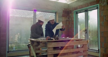 Tartışmalı inşaat işçileri, kapalı alandaki planları gözden geçirme, başlıklar, masadaki araçlar, işbirliği ve strateji, endüstriyel yapı projesi, takım çalışması