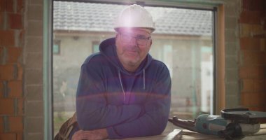 İnşaat işçisi inşaat halindeki tezgahta güvenle gülümsüyor, inşaat alanında güvenlik kaskı takıyor, rahat ve profesyonel atmosfer takıyor.