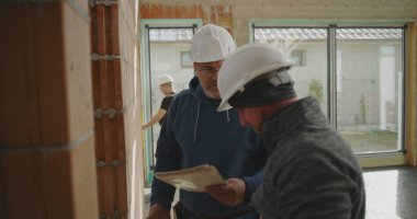 İnşaat işçisi tuğla duvarı ve mühendis gözlemi, inşaat sahasında açık duvarları ve geniş pencereleri olan takım çalışması