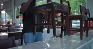 Restoran çalışanlarının elleri masaların üzerine ahşap sandalyeleri baş aşağı koyuyor, yemek servisinde iş gününün sonunun sinyalini veriyor.