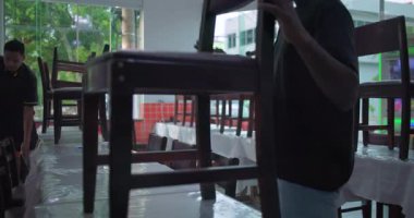 Restoran çalışanları günün sonunda masa üstüne sandalye istifliyor, doğal pencere ışığıyla günlük temizlik için yemek odasını hazırlıyorlar.