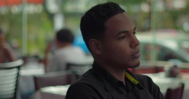 Sessiz yemek alanında oturan genç erkek restoran çalışanının yakın çekimi. Düşünceli bir ifade ve sakin bir tavırla pencereden dışarı bakıyor.