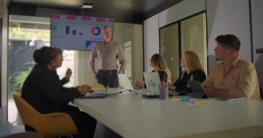 Çeşitli profesyoneller modern konferans odasında doğal ışık ile sunum izlerken, yönetici ekranda veri sunar