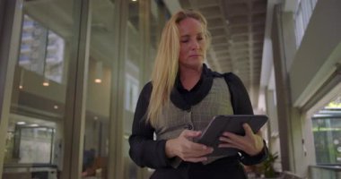Koridorda ciddi odaklanmış ifadeye sahip tableti inceleyen kadın, dijital içeriği kontrol ederken, çalışırken veya göreve hazırlanırken kıpırdamadan duruyor