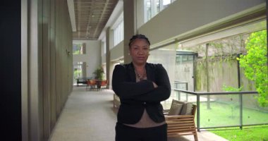 Afro-Amerikalı kadın, kollarını kavuşturup modern kurumsal koridorda gülümseyerek başarıyı temsil eden profesyonellik ve liderliğin sembolü olarak duruyor.