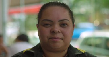 Latin garsonun kameraya sakince baktığı, restoranın yemek alanında penceresi ve gün ışığıyla durup arka planı aydınlattığı yakın plan.