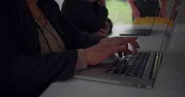 Ofis toplantısı sırasında dizüstü bilgisayarda yazı yazan eller kameranın, iş arkadaşlarıyla aynı masada çalışan Afrikalı Amerikalı iş kadınını yavaş yavaş ortaya çıkardığını gösteriyor.