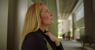 Yan bakış açısıyla, modern oturma ve pencerelerden süzülen yumuşak doğal ışık ile kurumsal koridorda elini göğsüne yaklaştıran bir kadın.