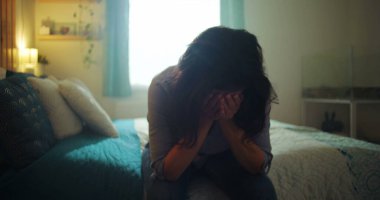 Yatakta oturan bir kadın, başını eğmiş, ellerini yüzünü kapatmış, umutsuzluk, keder ve kayıp, içsel ve derin bir duygusal an tarafından ezilmiş.