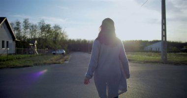 Sakin bir banliyö yolunda tek başına yürüyen bir kadın, huzurlu güneşli bir günde sakin bir mahalle ortamında, kameraya doğru döndü.