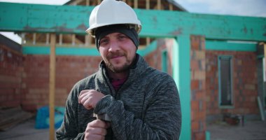 İnşaat işçisi elinde çekiçle inşaat alanında güvenle gülümsüyor takım çalışması ve inşaat halindeki konut yapısına olan bağlılığı profesyonel inşaatçı.