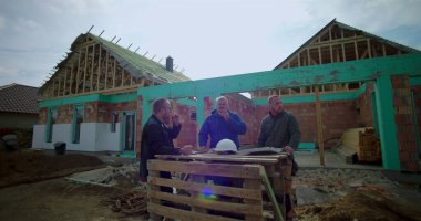 İnşaat alanında pizzayla öğle yemeği arası veren üç müteahhit, gelişigüzel toplanma, takım çalışması ve bağlanma, inşaat halindeki konut projesi.