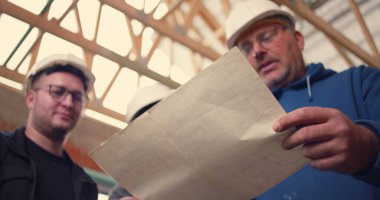 İnşaat ekibi, aktif bir iş sahasında proje tartışması yapan ayrıntılı yapı planlarına odaklanıyor.