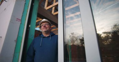 Dışarıya bakan, cam ve ahşap yapısı çerçeveli inşaat işçisi, aktif inşaat alanında sakin tavır.