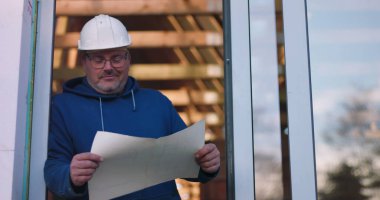 İnşaat planları, güvenlik kaskı ve gözlükleri inceleyen, proje detaylarını ciddi bir ifadeyle değerlendiren, kendinden emin ve profesyonel duruş sergileyen bir işçi.