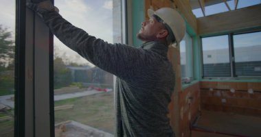 Kask takan inşaat işçisi, konut alanındaki pencere kurulumunu denetleyerek, kalite güvencesi için hassasiyet ve hizalamaya odaklanıyor