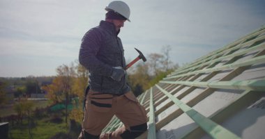 Çatı katında çekiç kullanan işçilerin yakın çekimi, konut inşaatı için ahşap yapı sağlanması, güvenlik malzemesi giyilmesi, dışarıda kaliteli işçilik.