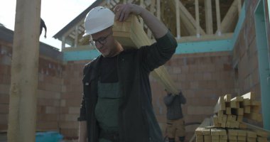 Odaklanmış inşaat işçisi omuzlarında odun destesi taşır, konut inşaatı projesinde takım çalışması, marangozluk görevlerinde kendini adama ve güç