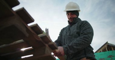 İnşaat işçisi çekiç kullanıyor, yakın çekim yapıyor, konut inşaatında marangozluk yapıyor, el aletine odaklanıyor, arka plandaki yapı iskeletine odaklanıyor.