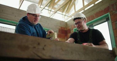 İnşaat işçileri inşaat sahasında odun testeresi, inşaat iskeletinde takım çalışması, bir işçi keserken diğeri yardım ediyor, hassasiyet ve güvenliğe odaklanıyor