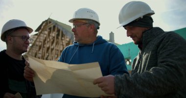 İnşaat işçileri inşaat alanındaki planları gözden geçiriyorlar, inşaat planlamasında takım çalışması, projeyi tartışan sektör profesyonelleri, inşaat geliştirmede işbirliği