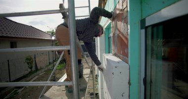 Dış duvardaki yalıtım panelinin temizleme yüzeyi, güvenlik miğferi ve eldiveni olan inşaat işçisi, konut yenileme, yakın hizalama