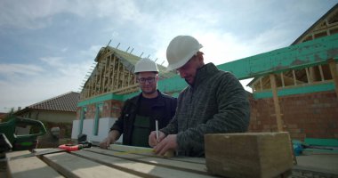 Ahşap tahtaları, takım çalışmasını ve işbirliğini, kalın şapkaları, aletleri, inşaat çalışmalarını ölçmek ve işaretlemek üzere yeni bir ev projesinde birlikte çalışan inşaatçıların yakın plan fotoğrafları.