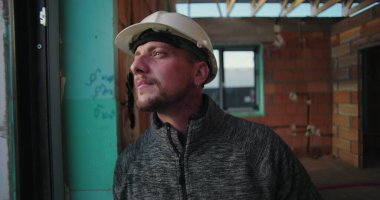 Dışarıya bakan genç inşaat işçilerinin yakın çekimi, sert şapkalı, odaklı ifade, kısmen inşa edilmiş tuğla duvarlı bir binanın penceresinin yanında duruyor.