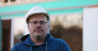 İnşaat işçisi, inşaat alanında ciddi bir ifadeyle ileriye bakıyor. Yüze odaklanıyor, inşaat projesi devam ediyor, açık havada çalışıyor.