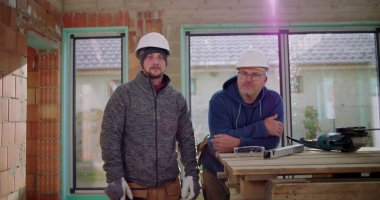 Kısmen inşa edilmiş yapının yanında duran iki inşaat işçisi, güvenlik kaskı takıyorlar, inşaat sahasında takım çalışması, inşaat endüstrisi, gündüz ayarı