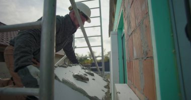 İnşaat işçisi, yalıtımlı paneli yapıştırıcıyla kaldırıyor. İnşaat alanındaki duvar döşemesi, yapı iskelesi ve arka plandaki tuğla duvar için hazırlanıyor.